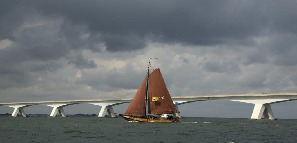 Een oude Hoogaars vaart voor een lange brug