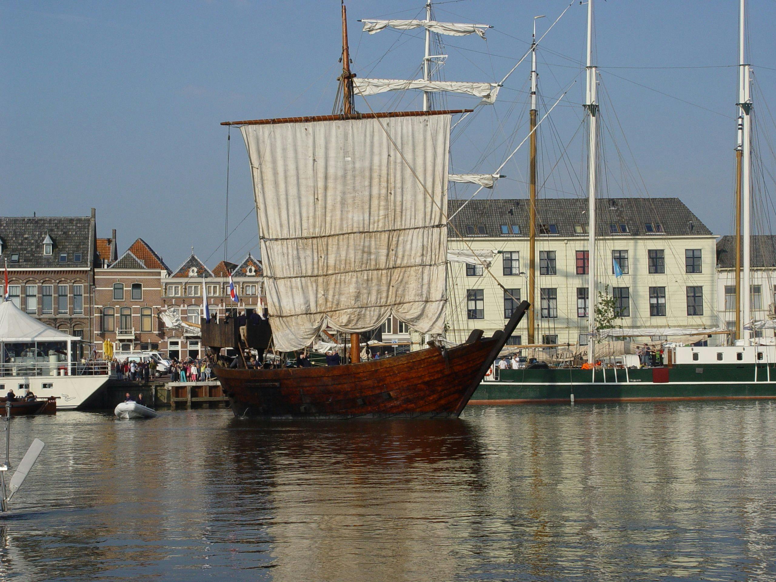 Een oude boot van hout en met een wit zeil van de vereniging Kamper Kogge vaart de haven in