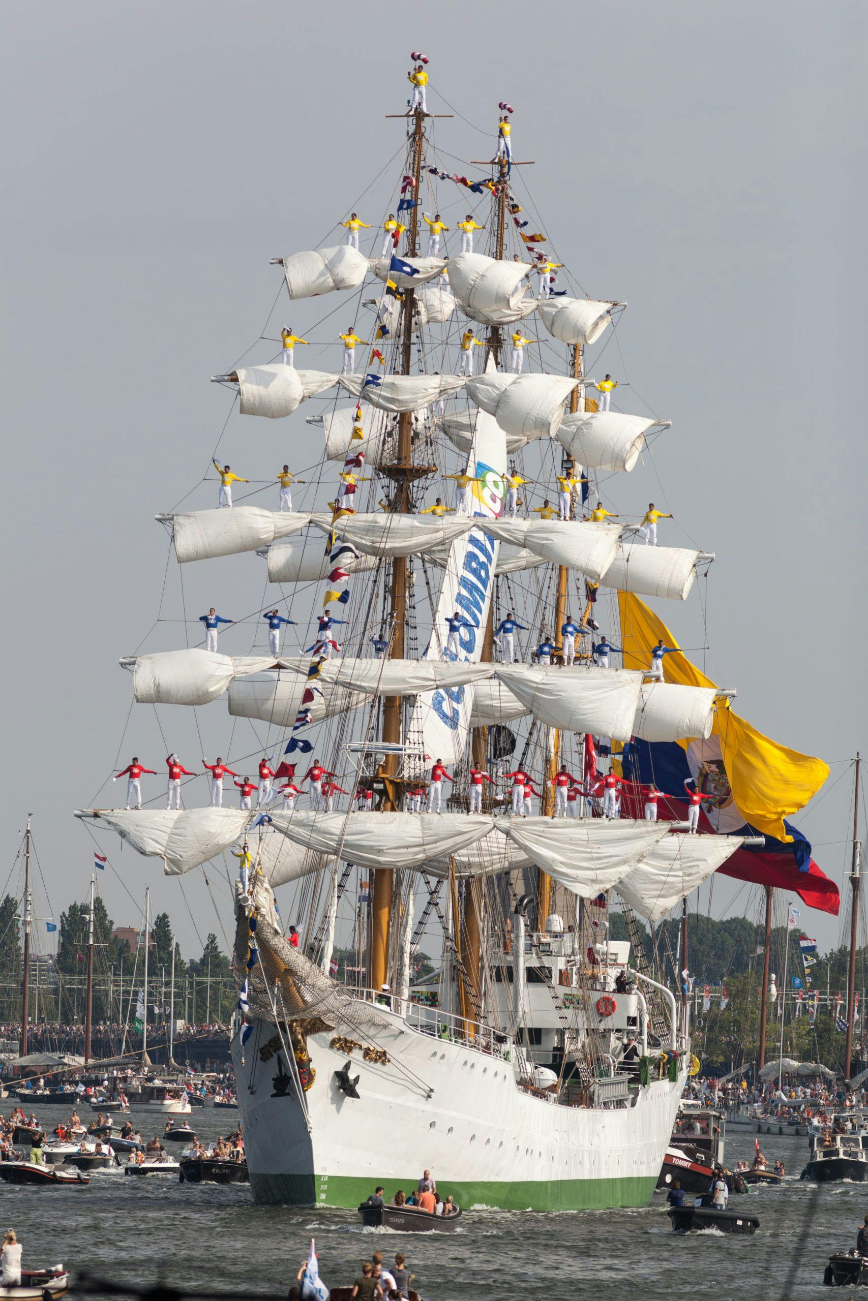 Bemanning van de ARC Gloria staan in de masten van het schip terwijl het de haven in vaart